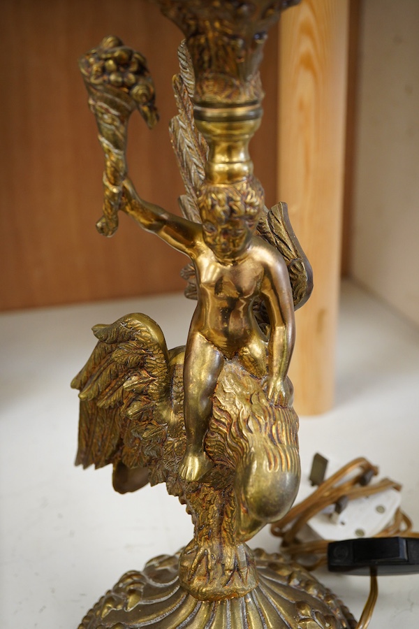A brass three light table lamp with green toleware shade, another similar table lamp and a brass glass shaded lamp with a putti riding on the back of an eagle, (3)